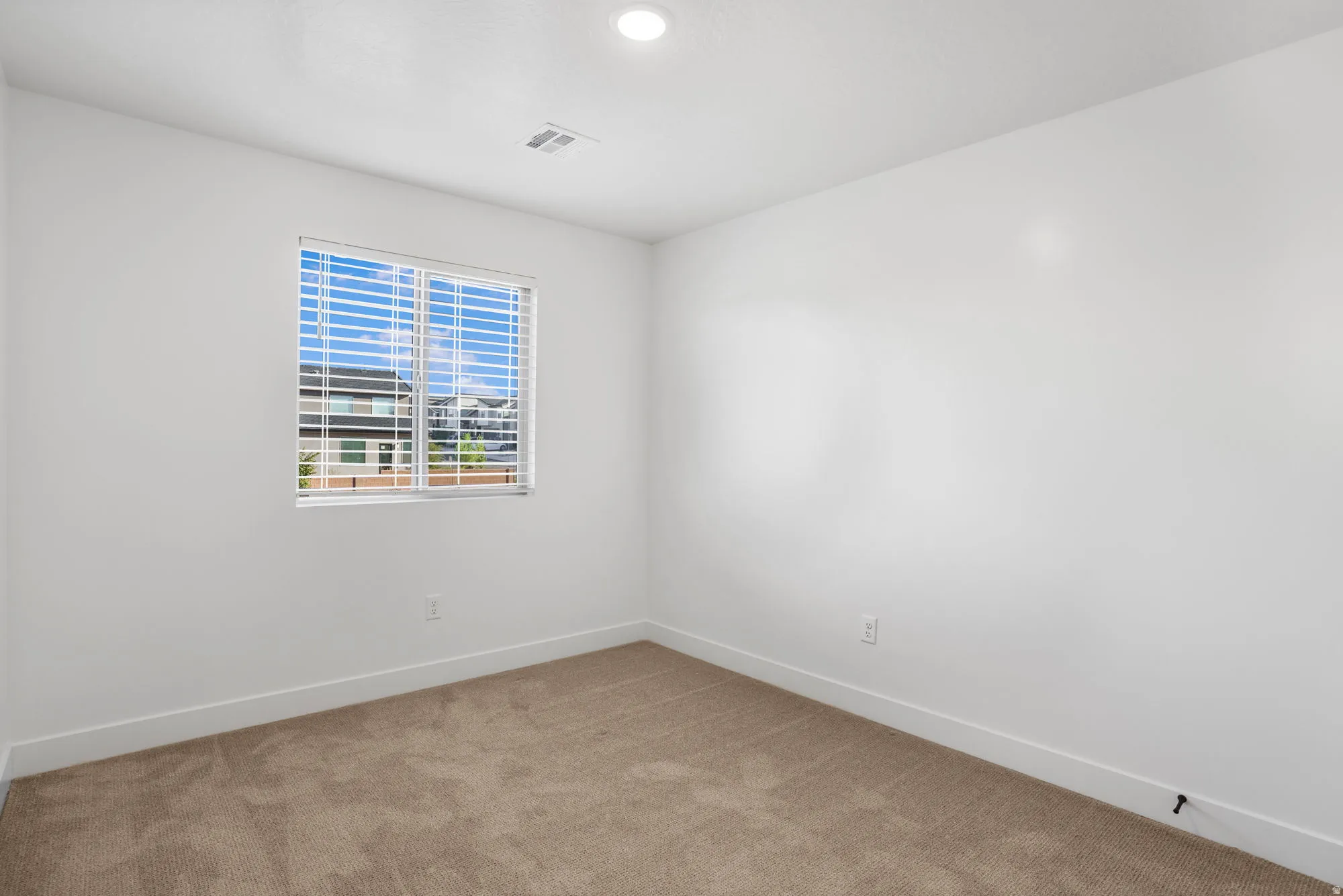Bright secondary bedroom featuring neutral carpeting, clean white walls, and a large window with plantation shutters offering natural light and outdoor visibility