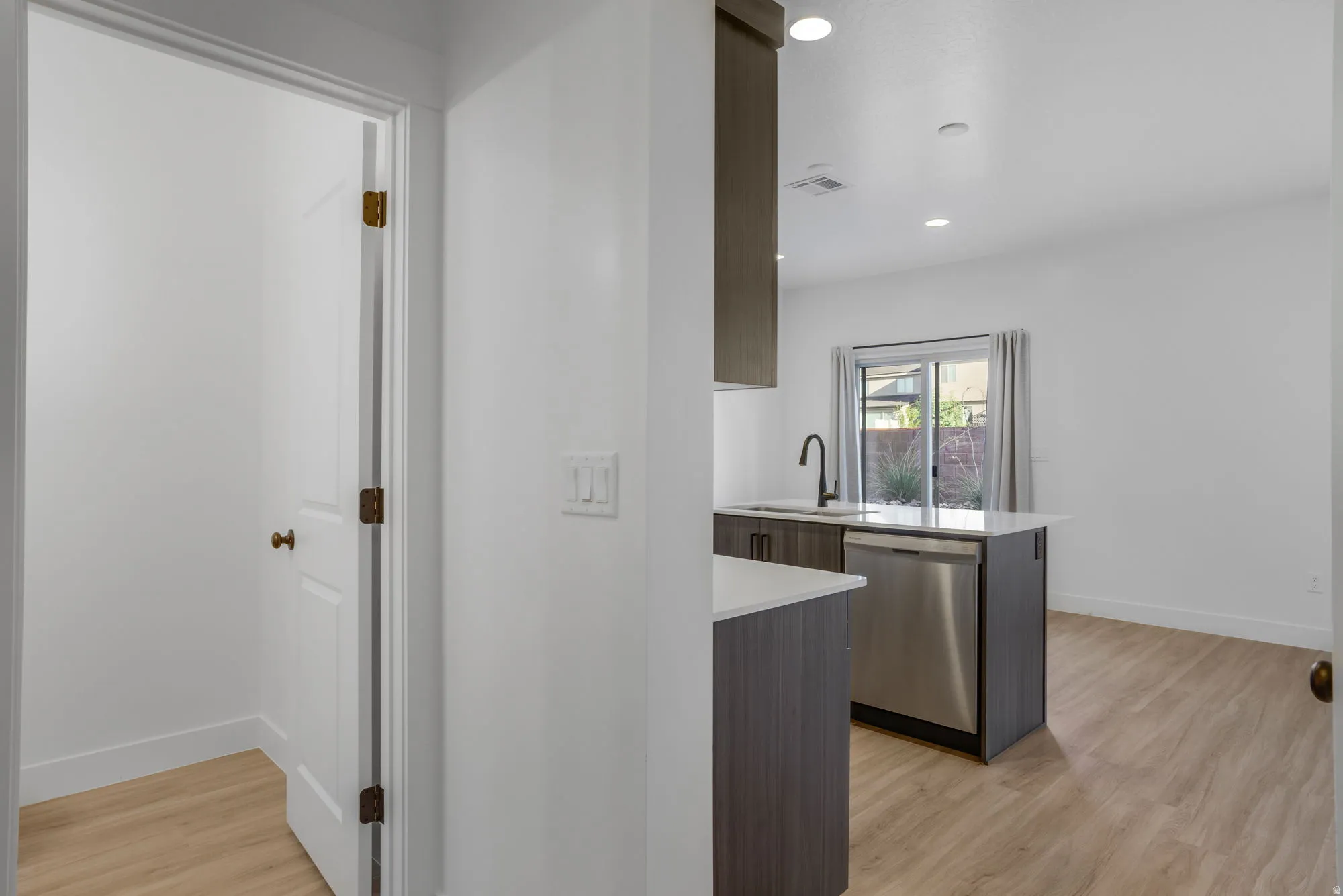 Modern kitchen with dark wood-finish cabinetry, light-toned countertops, and a stainless steel dishwasher