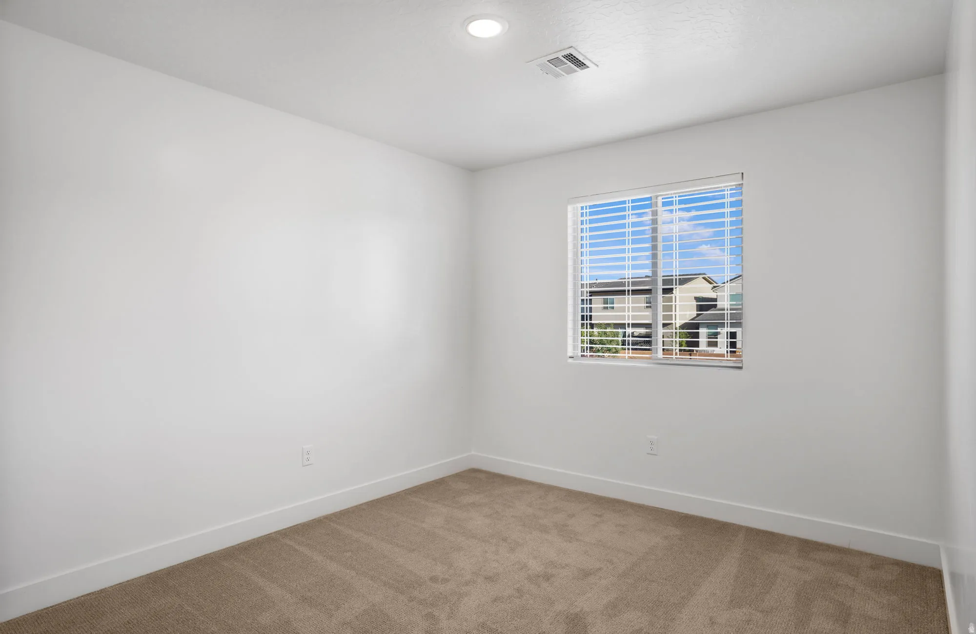 Bright bedroom with neutral wall finishes, recessed ceiling lighting, and a single window with plantation shutters framing natural light