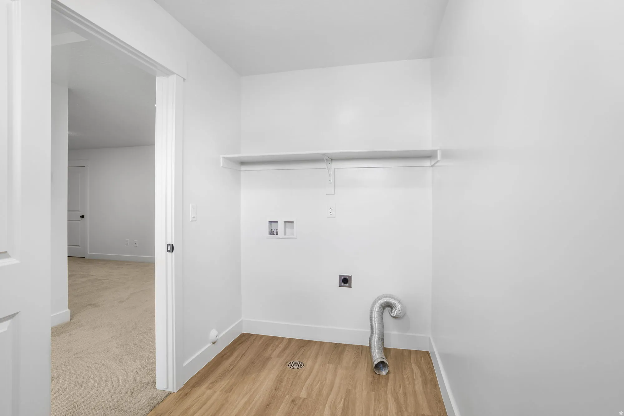 Laundry area featuring wood-finish flooring, white walls, and a built-in shelf