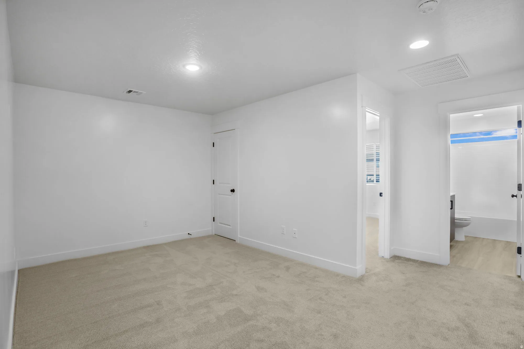 Spacious bedroom featuring neutral white walls, recessed ceiling lighting, and neutral-tone carpet flooring