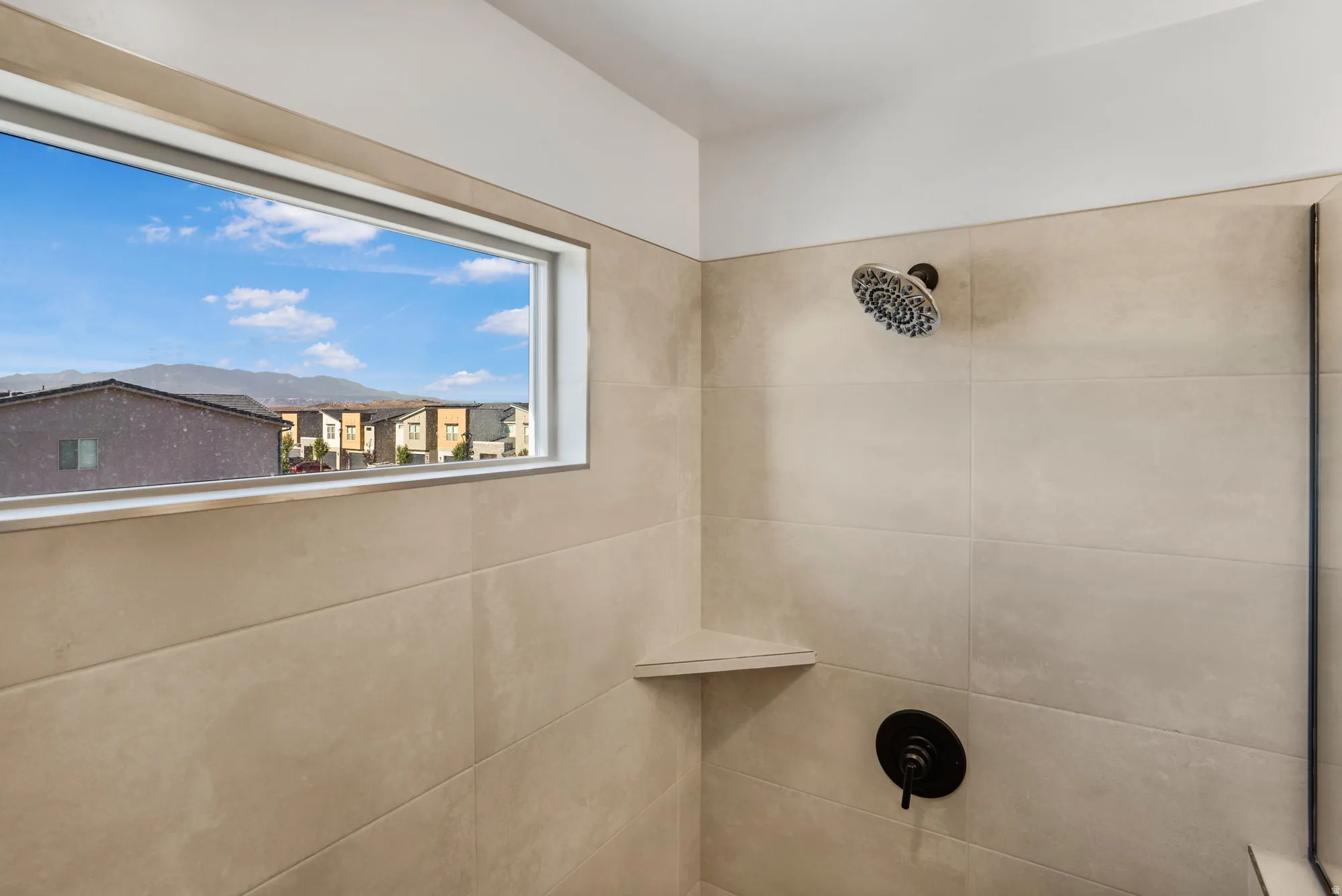 Shower enclosure featuring large format tile walls, a built-in corner shelf, and a horizontal window