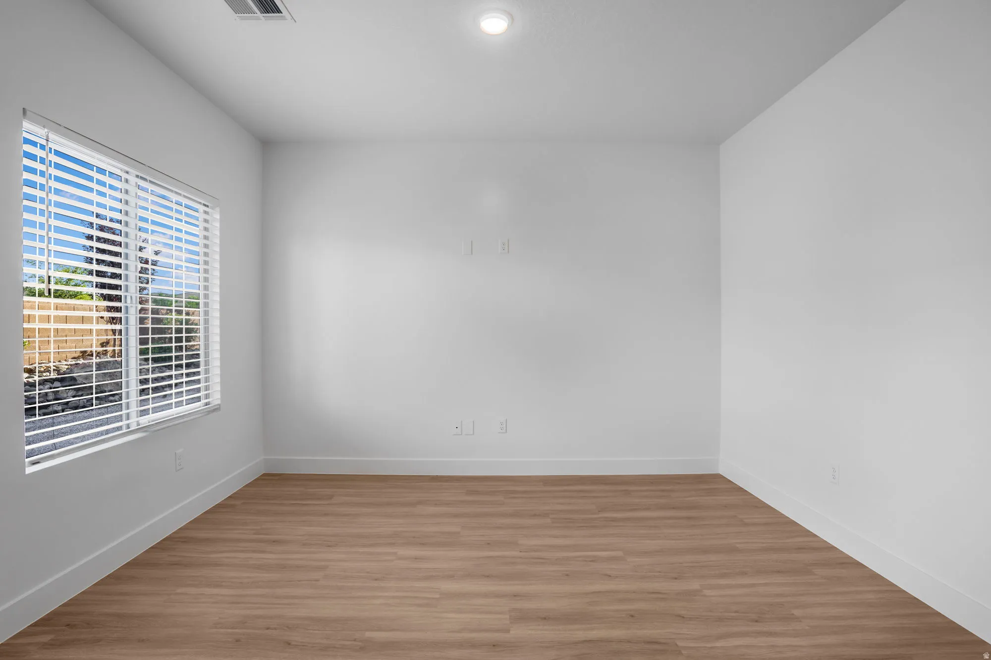 Room featuring wood-finish flooring, white baseboards, and a window with blinds