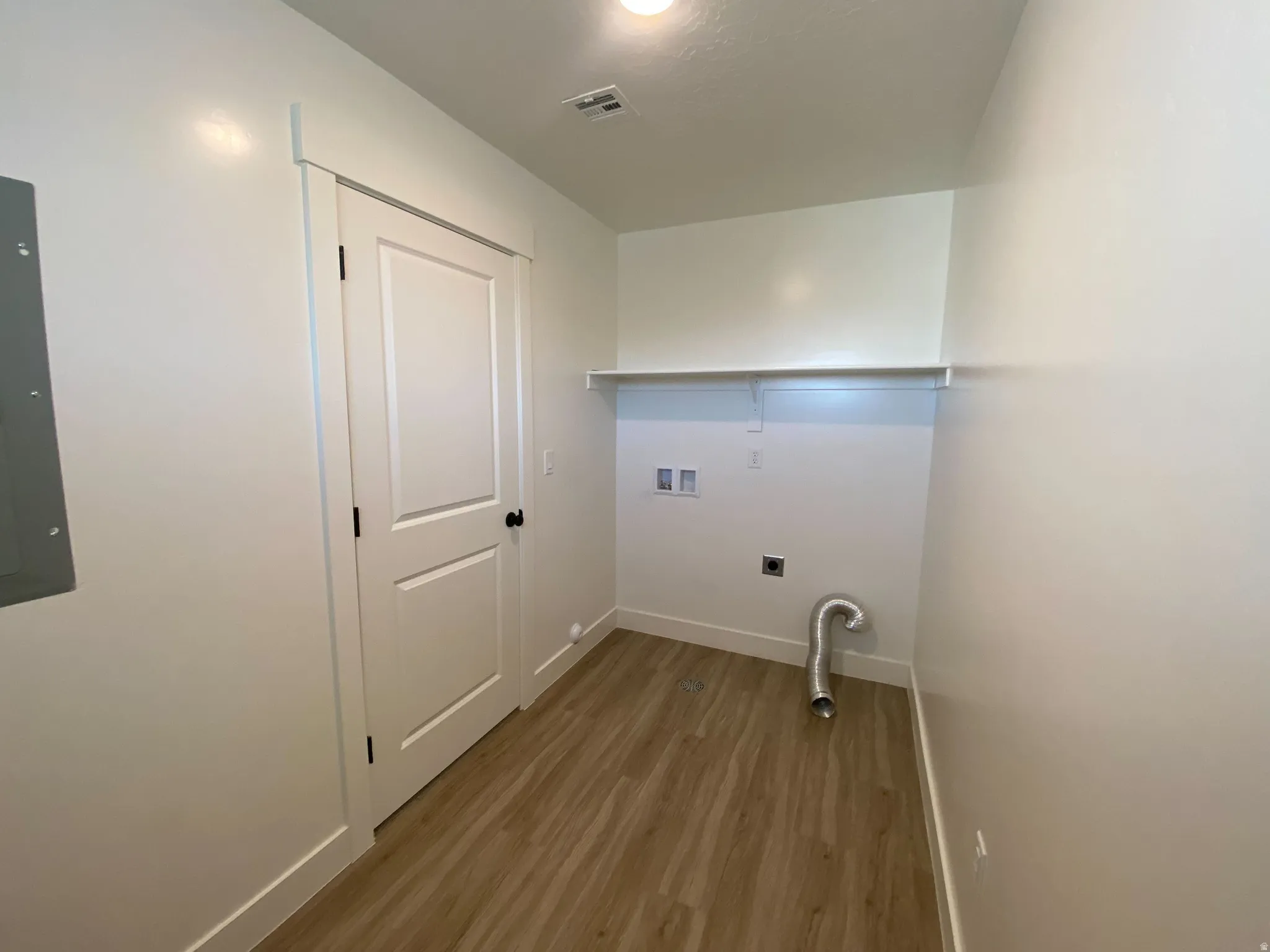 Laundry area featuring wood-finish flooring, white walls, and a built-in shelf