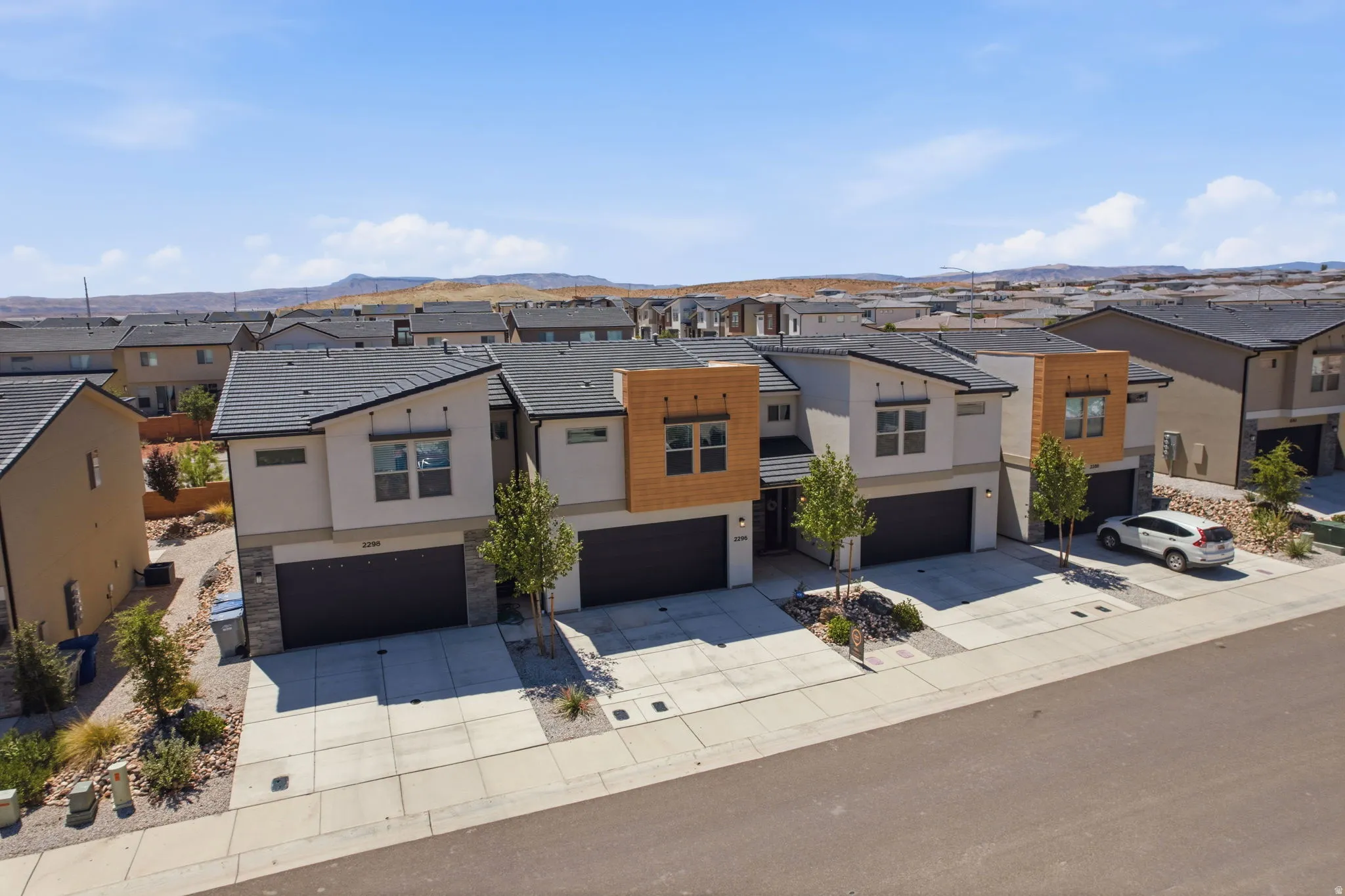 Modern townhome exteriors featuring light stucco, dark tiled roofs, and stone veneer accents