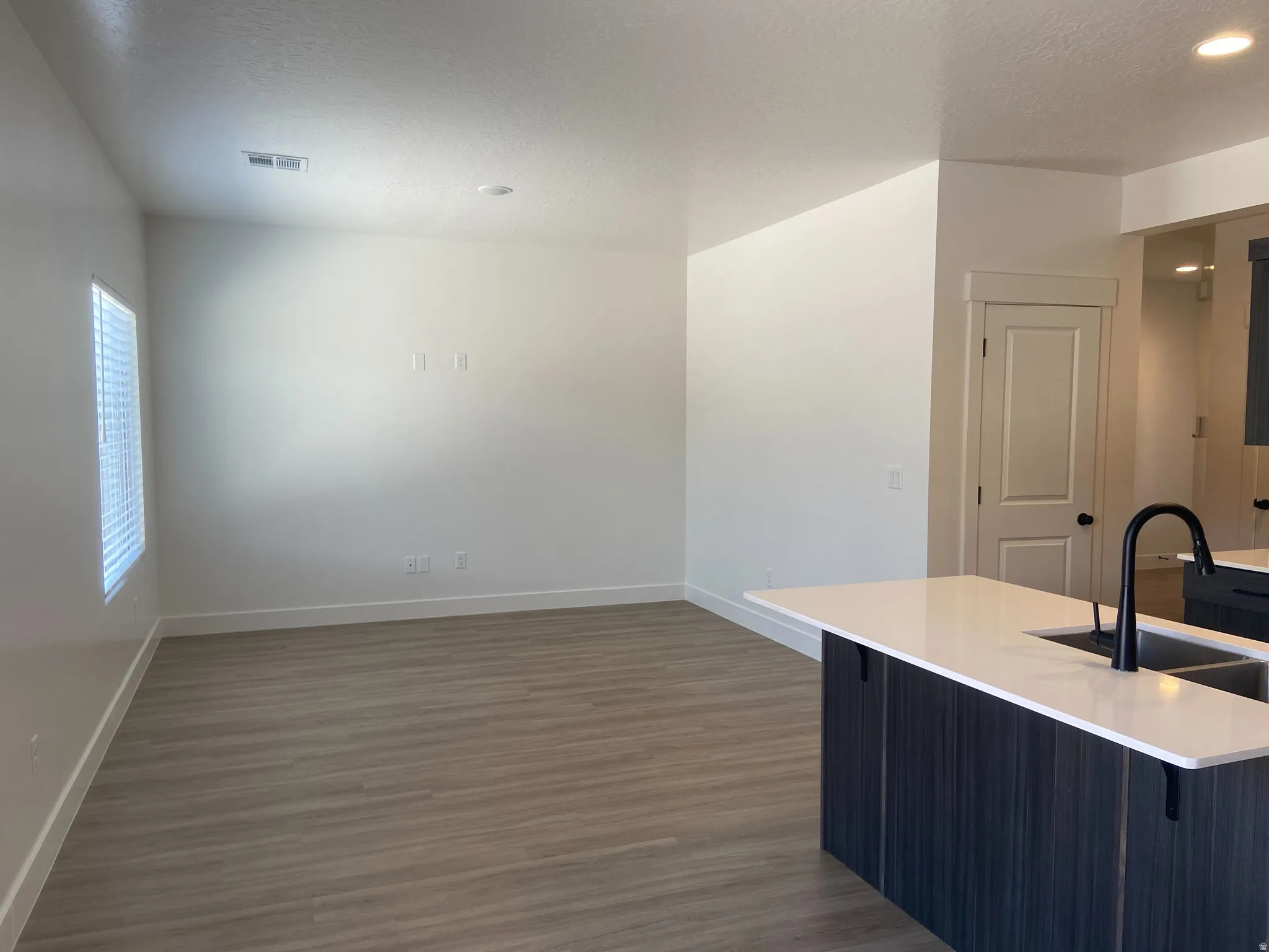 Open-concept living space featuring wood-finish flooring, recessed lighting, and a window with blinds