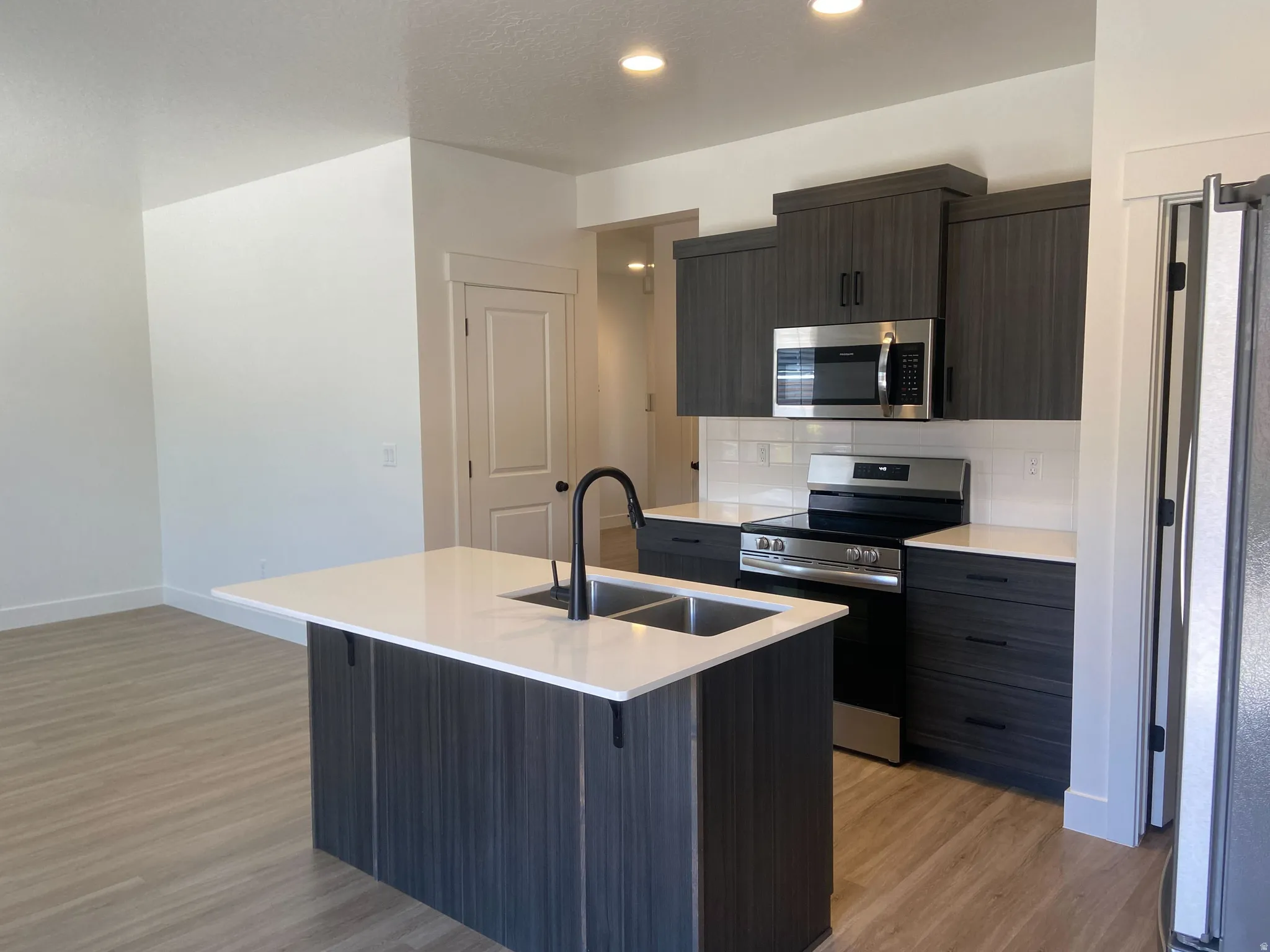 Modern kitchen featuring dark wood-finish cabinetry, light countertops, and stainless steel appliances
