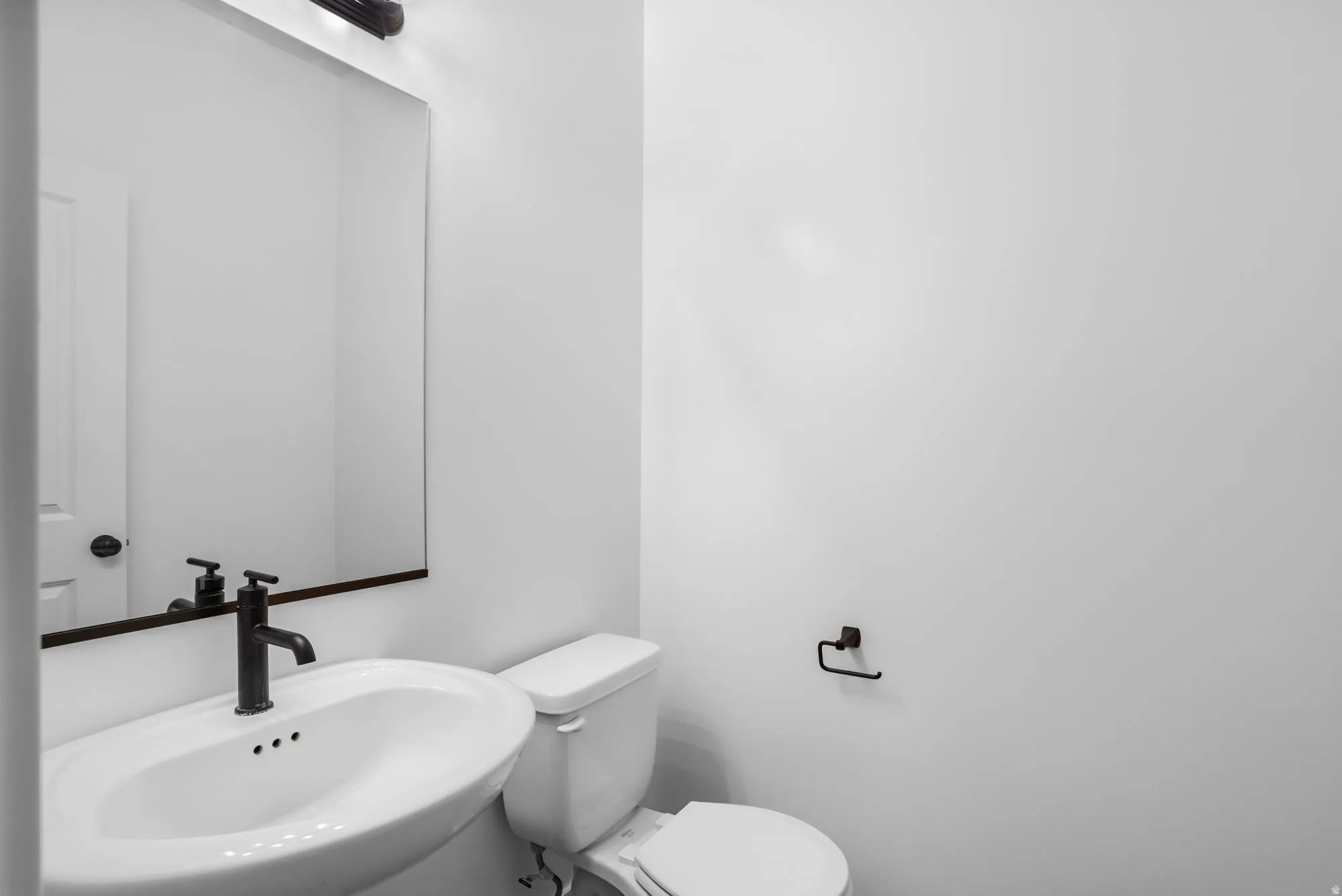 Pedestal sink with a matte black faucet, framed mirror, and coordinating overhead light fixture