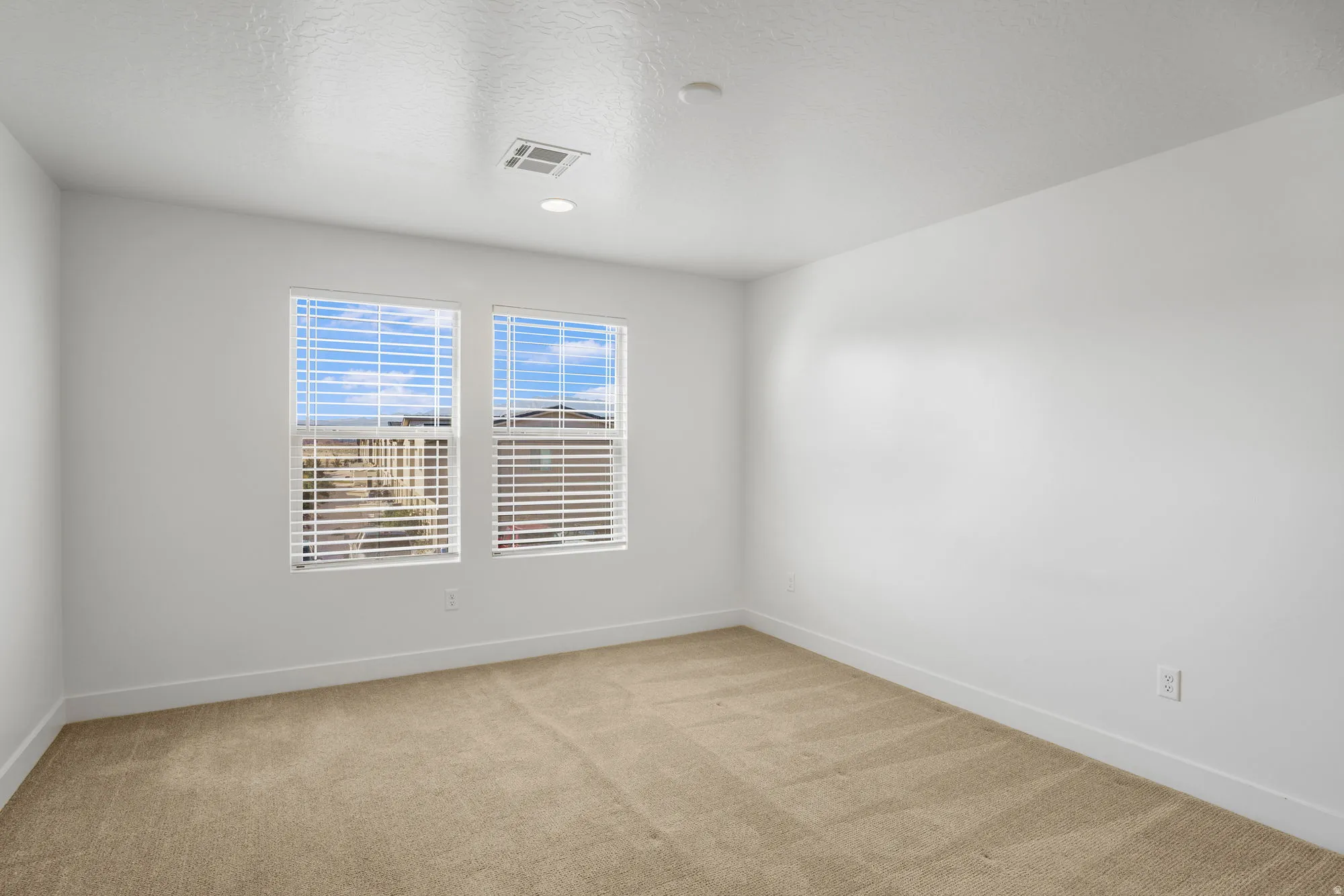 Bright room featuring two windows with white blinds, neutral carpeting, white walls, and recessed lighting
