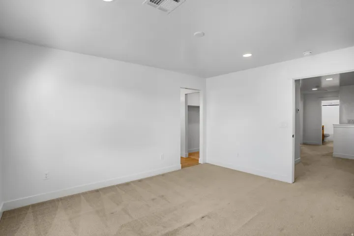 Spacious interior room featuring clean white walls, recessed ceiling lighting, and neutral wood-finish flooring