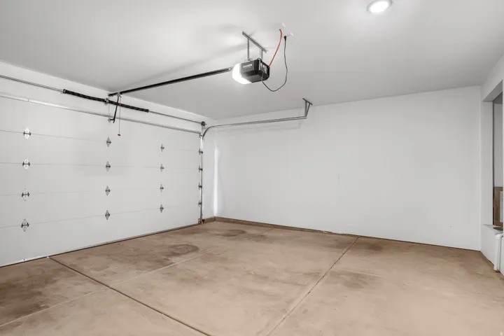 Spacious garage featuring a concrete floor, white painted walls, and a white paneled garage door with an automatic opener