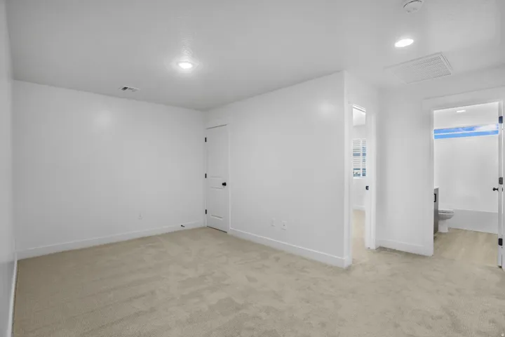 Spacious bedroom featuring neutral white walls, recessed ceiling lighting, and neutral-tone carpet flooring