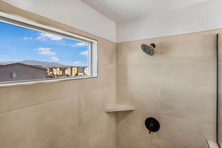 Shower enclosure featuring large format tile walls, a built-in corner shelf, and a horizontal window