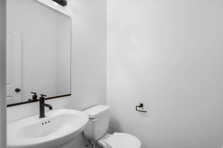 Pedestal sink with a matte black faucet, framed mirror, and coordinating overhead light fixture