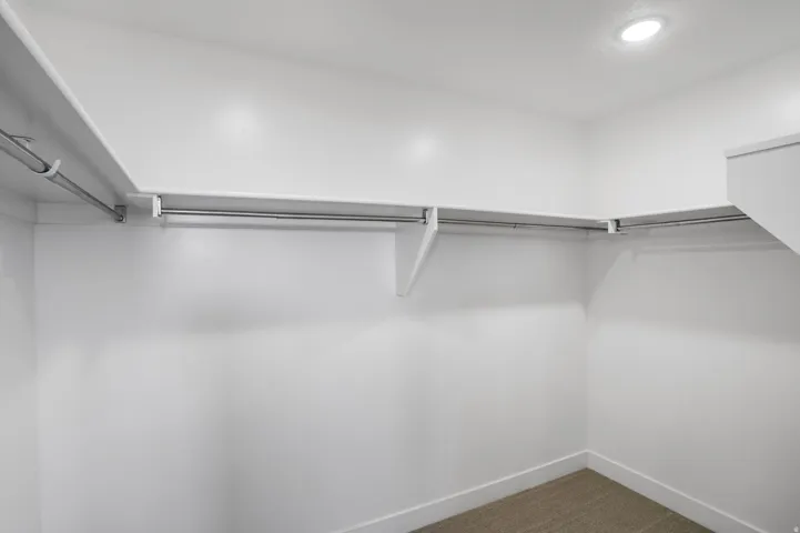 Spacious walk-in closet featuring white walls, ample shelving, and multiple clothing rods