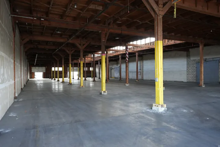 Expansive industrial interior featuring a concrete floor, exposed wooden beam ceiling, and multiple support columns