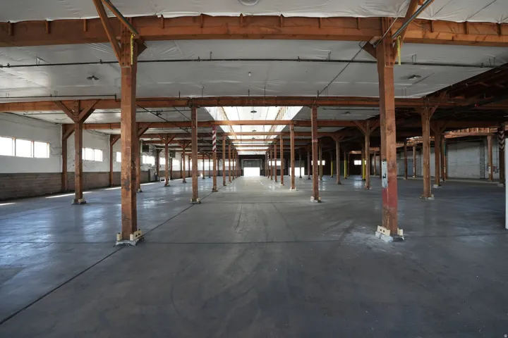 Expansive open interior space with concrete flooring, exposed wood beam ceiling, and skylights providing natural illumination