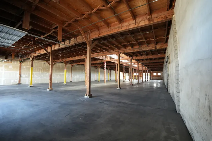 Expansive commercial interior featuring exposed wood beam ceilings, numerous structural wood columns, and a concrete floor