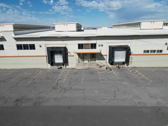 Industrial building featuring two loading docks with overhead doors, a paved parking area, multiple windows, and a flat roofline