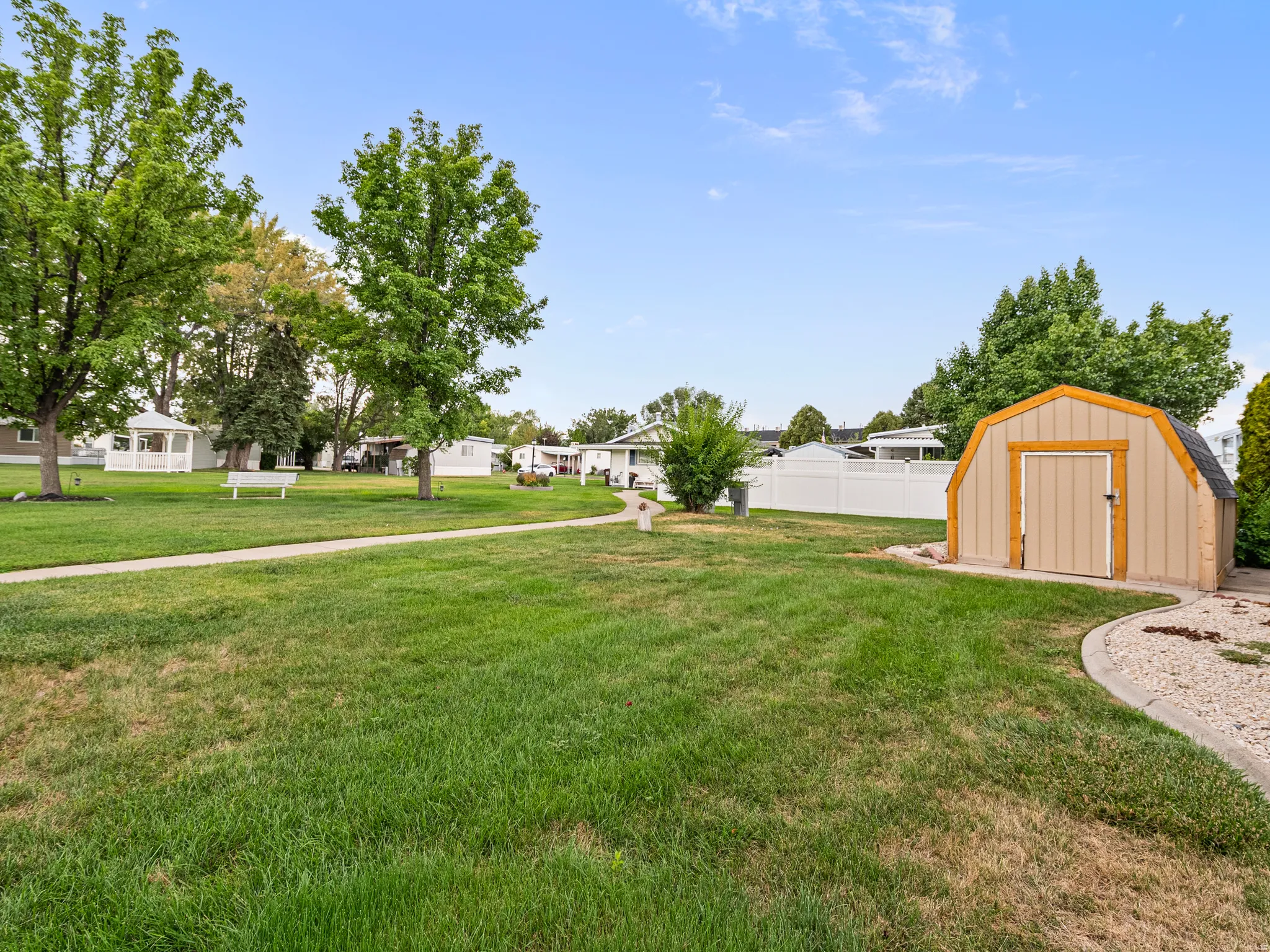 Expansive green space featuring a curved pathway, a freestanding storage shed, and mature trees