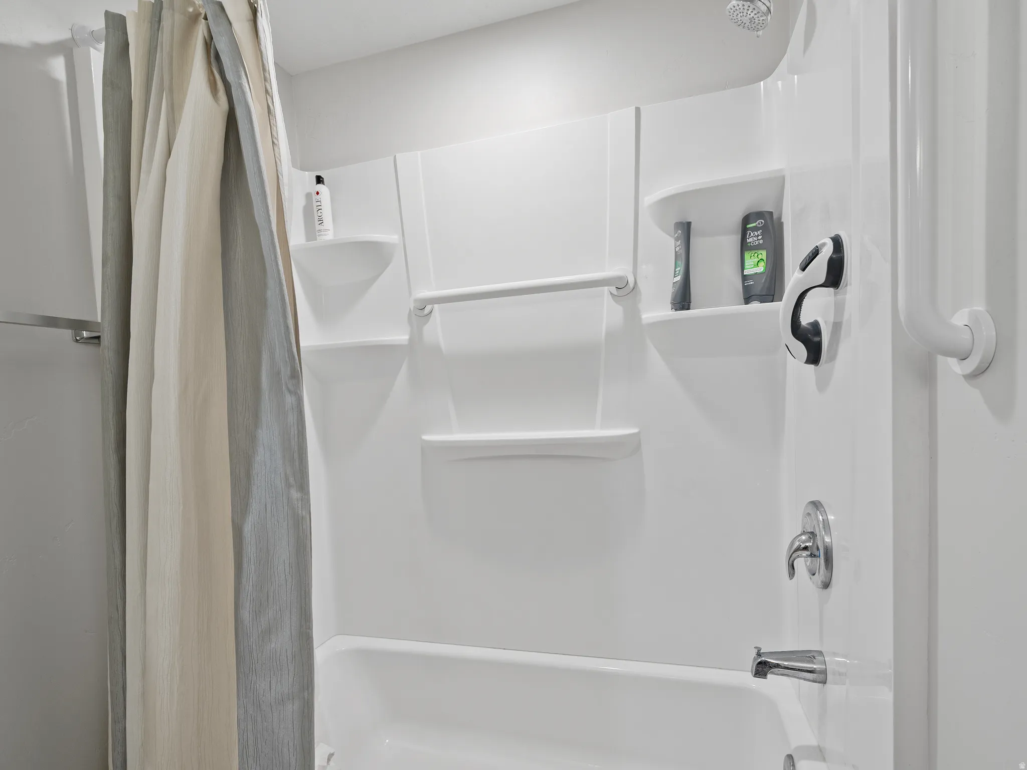 White shower-over-tub combination with integrated shelving, chrome fixtures, and a showerhead