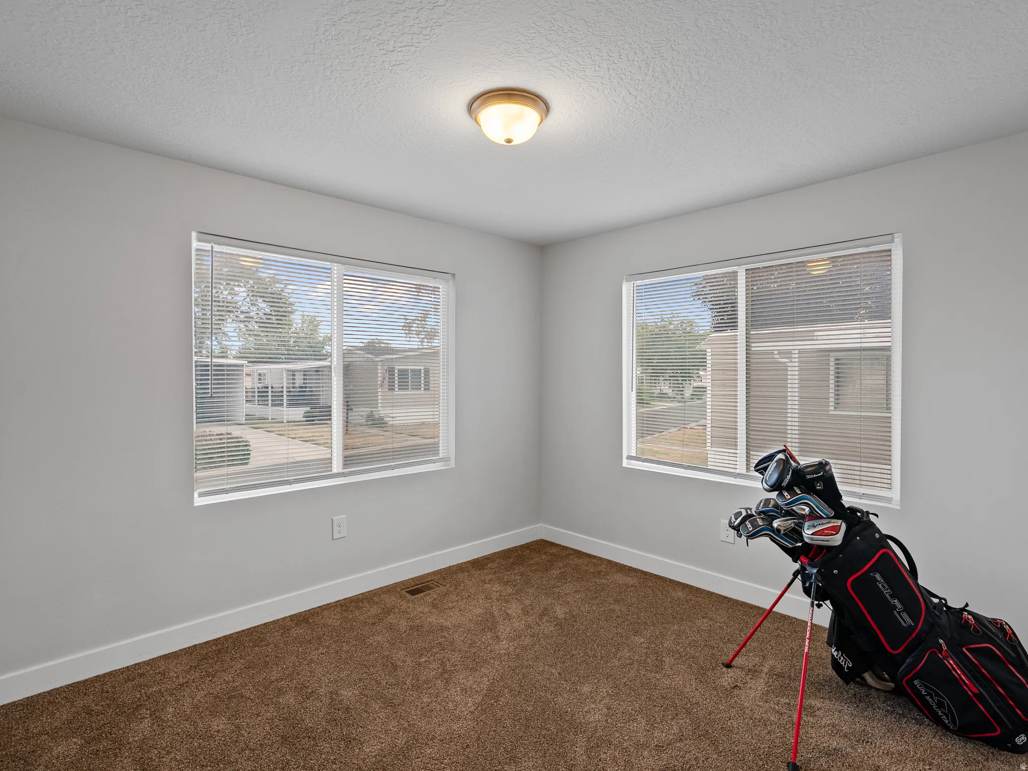Bright room featuring two windows with horizontal blinds, neutral wall paint, and a textured ceiling