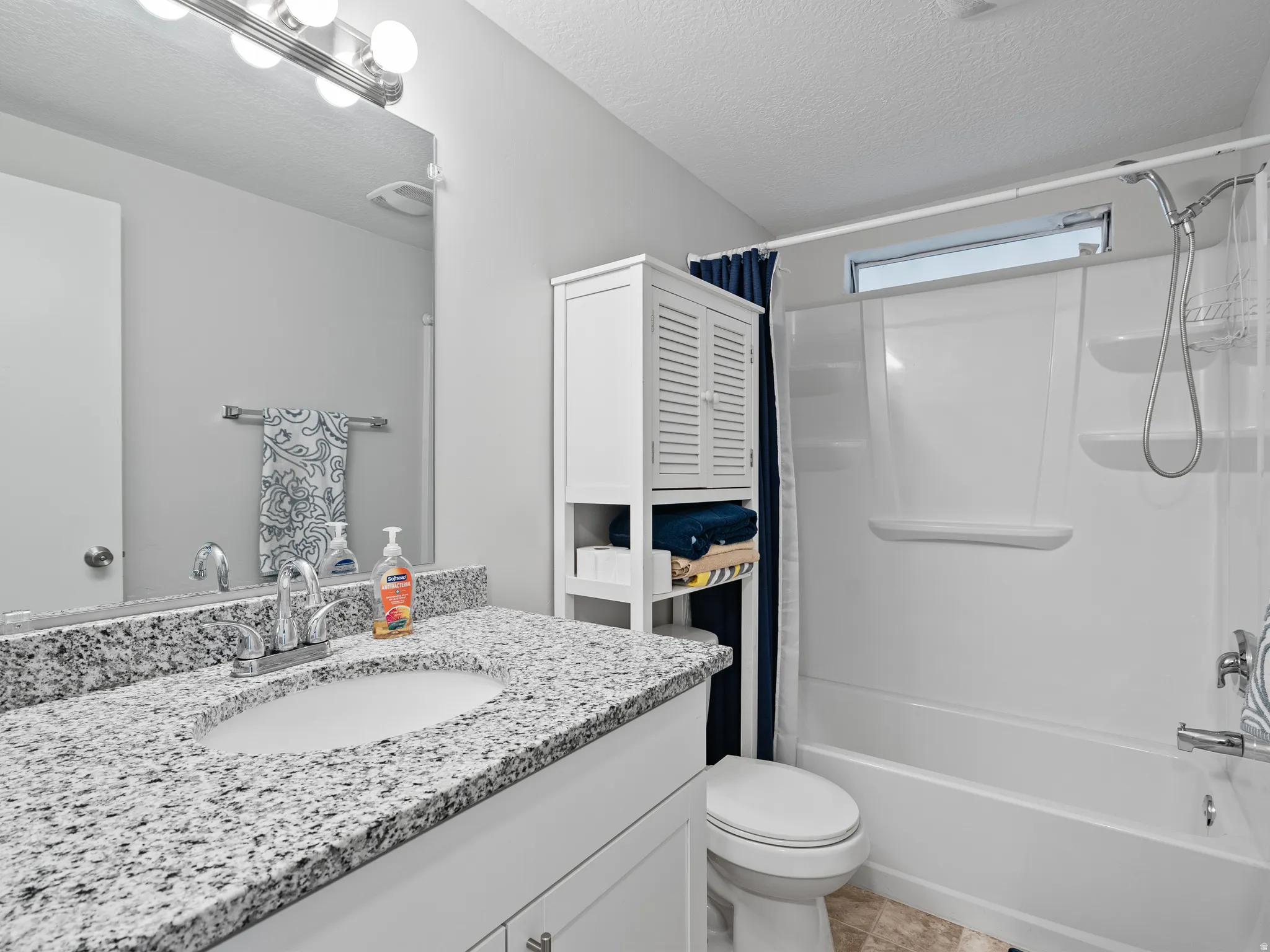 Bathroom featuring a granite-look countertop, undermount sink, white vanity cabinetry, and a shower-tub combination with a transom window