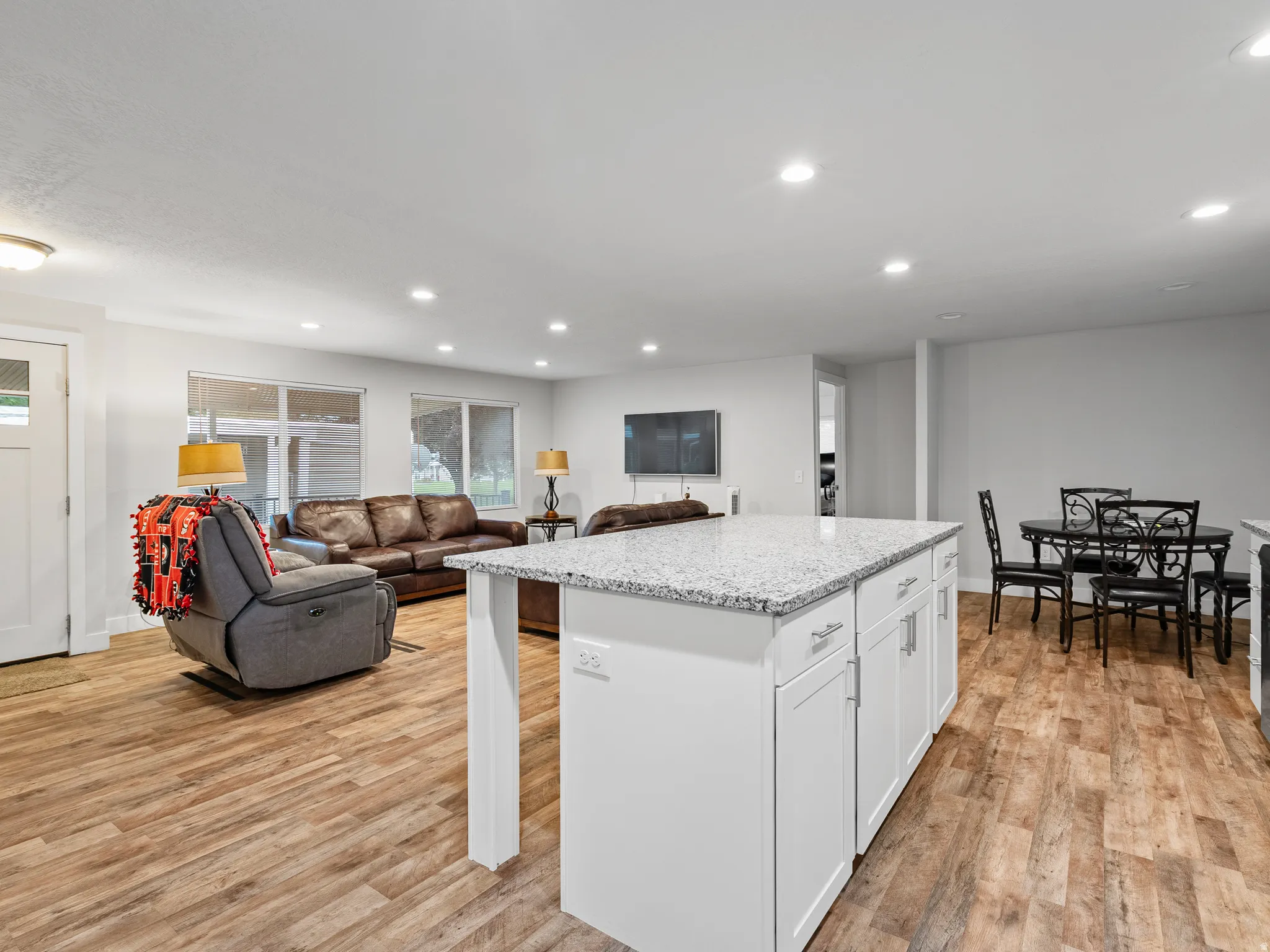 Spacious open-concept area featuring a white kitchen island with a light-toned countertop, wood-finish flooring, and recessed lighting