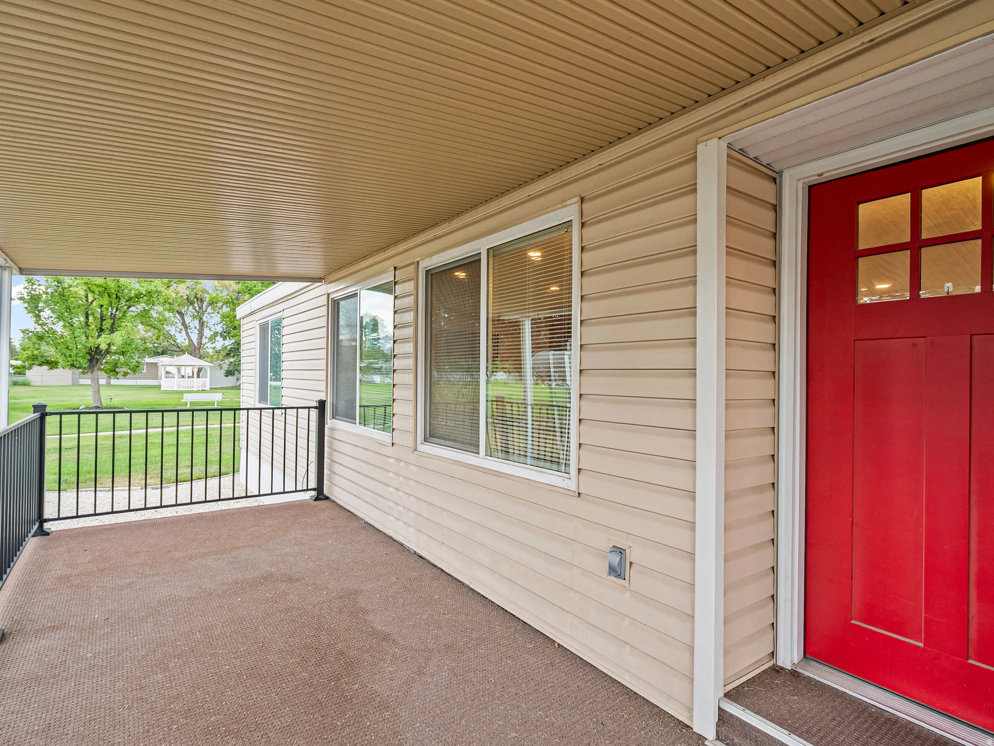 Covered front porch featuring a red entrance door with glass inserts, tan siding, and a black metal railing