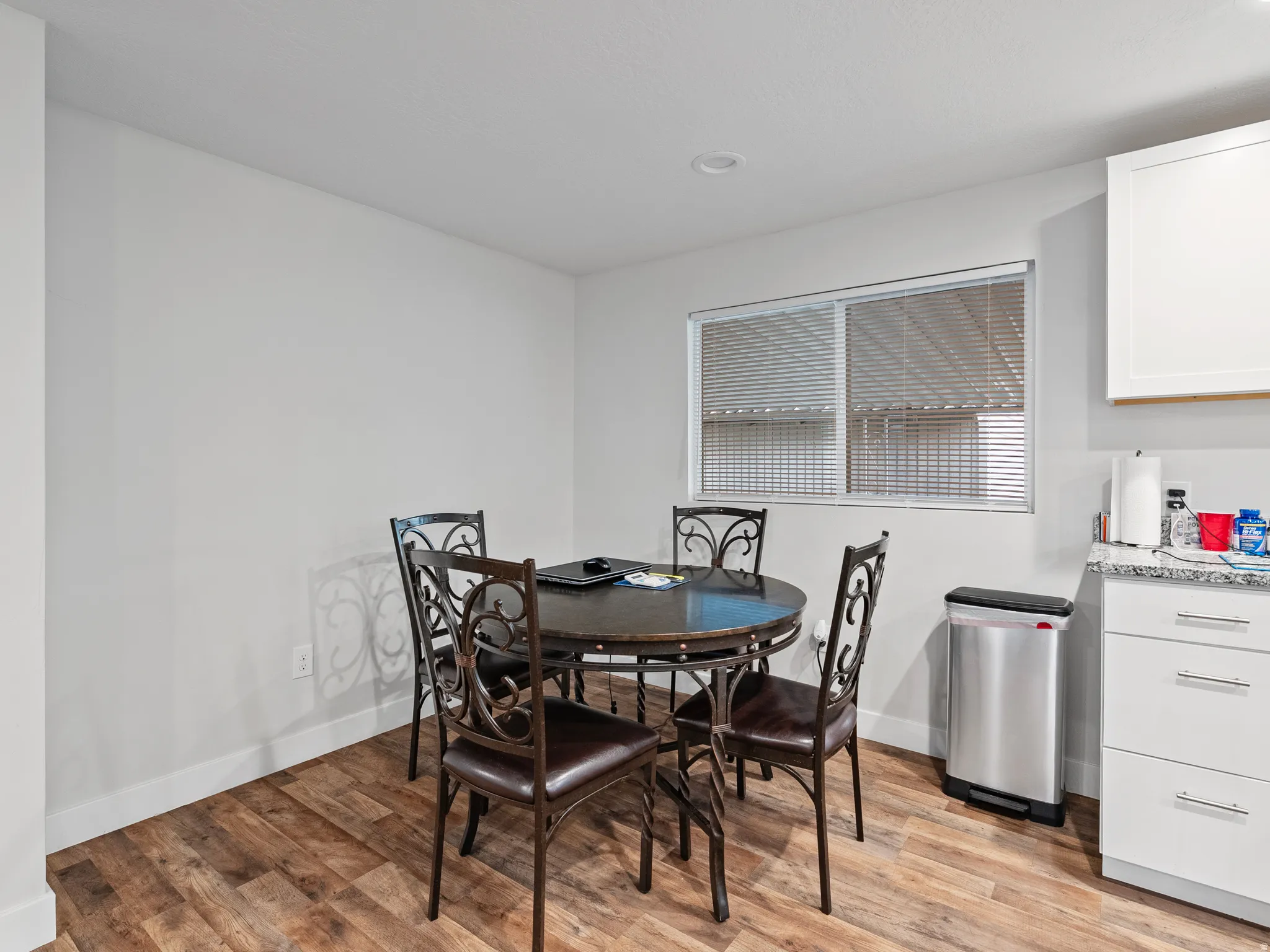 Light-filled dining area featuring wood-finish flooring, white walls, and a large window with horizontal blinds