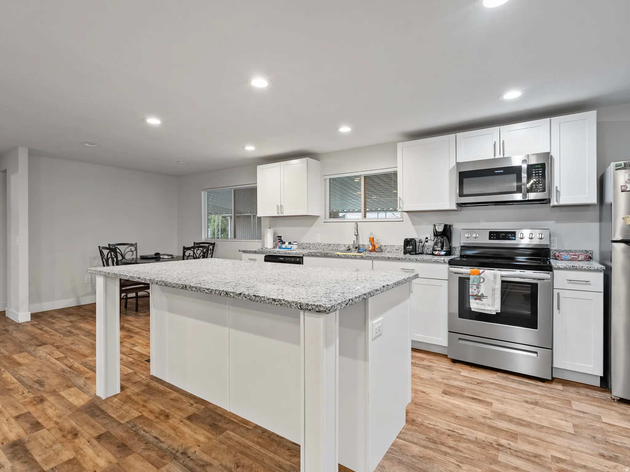 Kitchen featuring a central island with a speckled countertop, white cabinetry, stainless steel appliances, and wood-finish flooring