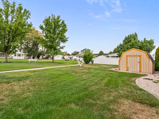 Expansive green space featuring a curved pathway, a freestanding storage shed, and mature trees