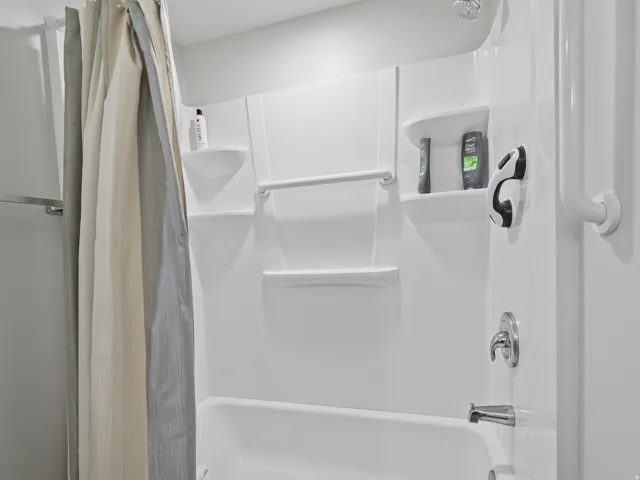 White shower-over-tub combination with integrated shelving, chrome fixtures, and a showerhead