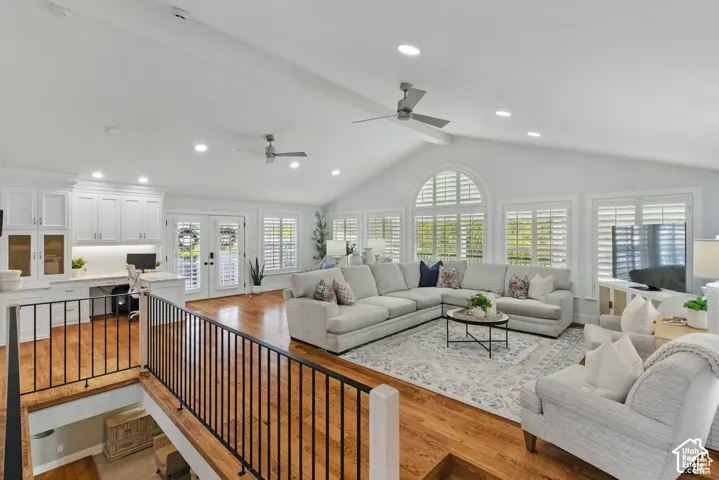 Vaulted ceiling living area featuring wood-finish flooring, plantation shutters, French doors, and built-in white cabinetry with a desk area