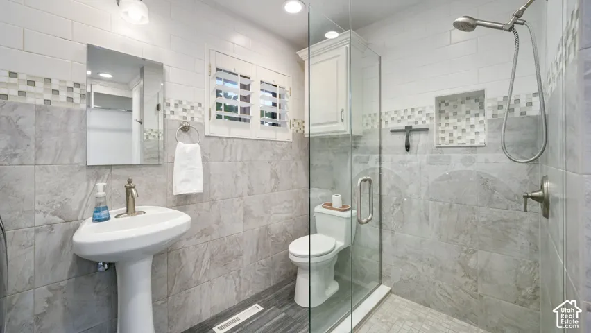 Guest-Bathroom featuring a pedestal sink, a glass-enclosed shower, and a white shuttered window