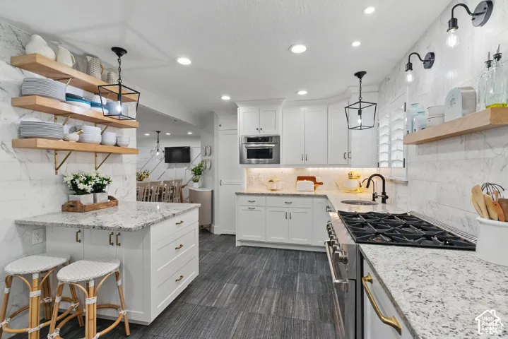 Open-concept kitchen featuring white shaker cabinetry, light-toned granite countertops, a gas range, and a full-height marble-look tile backsplash