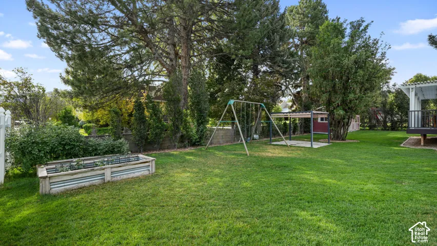 Expansive green lawn featuring a raised garden bed with metal accents, mature trees, and a white picket fence