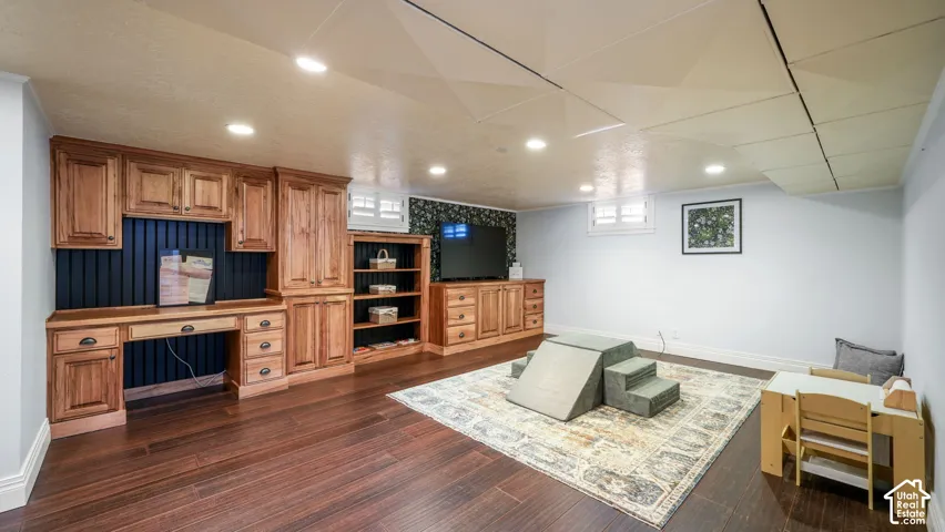 Expansive room featuring rich wood-finish flooring, recessed lighting, and a built-in desk with cabinetry and shelving
