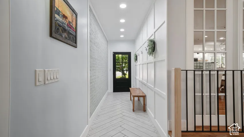 Entryway featuring wood-finish herringbone flooring, paneled wall detailing, recessed lighting, a brick-textured accent wall, and a dark-framed glass-paned door