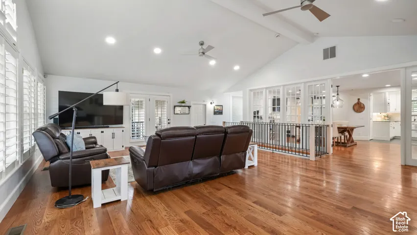 Spacious living area featuring polished wood-finish flooring, a vaulted ceiling, recessed lighting, and plantation shutters