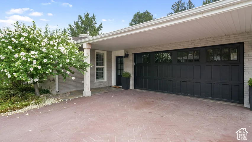 Brick exterior featuring a herringbone pattern paver driveway, a covered entry, and a multi-pane garage door