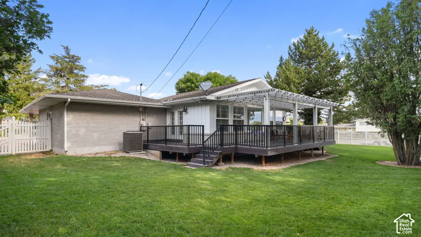 Expansive green lawn with a spacious deck featuring dark railings, steps, and a white pergola