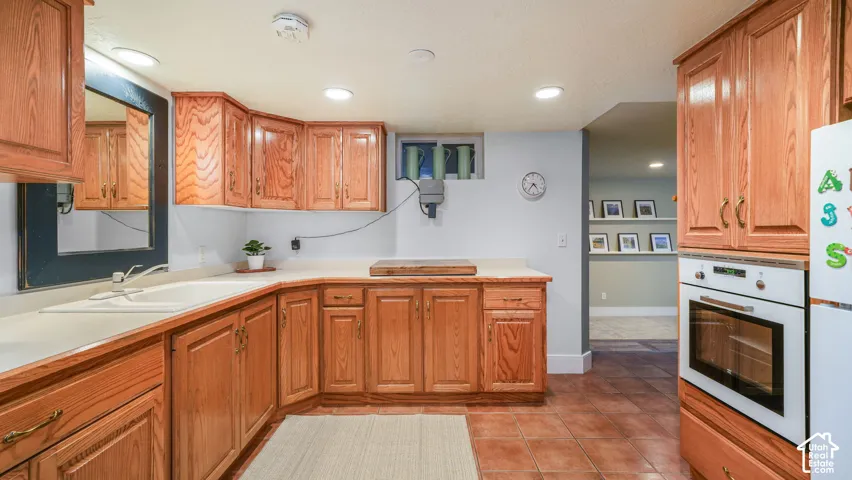 Kitchen featuring extensive wood cabinetry, light-toned countertops, built-in oven, and a corner sink