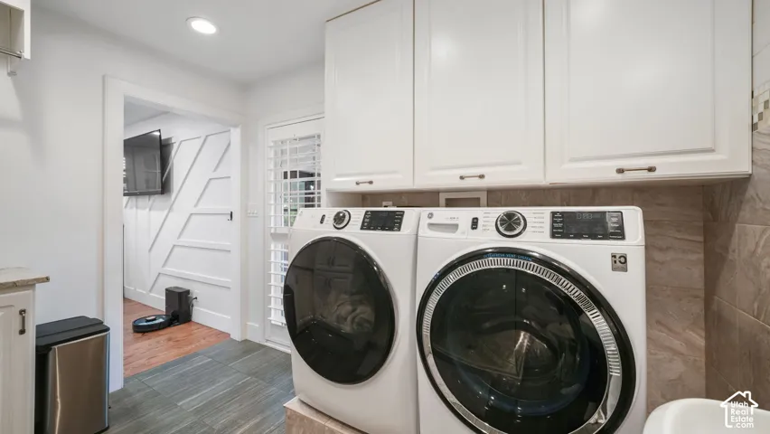 Laundry area featuring white cabinetry, stone-finish tile flooring, a side door with white shutters, and a counter space with an under-counter cabinet