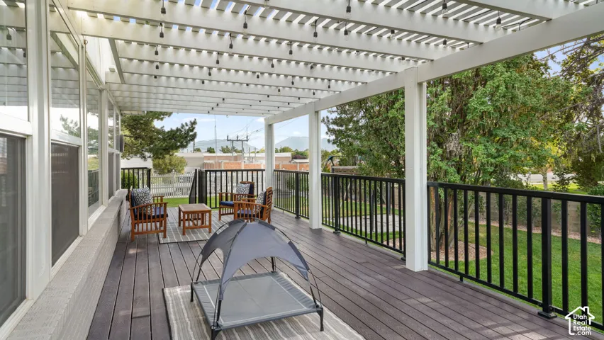 Expansive composite deck featuring a slatted pergola with integrated lighting, durable black metal railings, and a verdant lawn perimeter