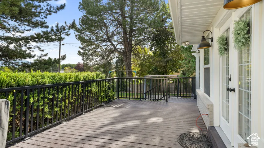 Spacious exterior deck featuring wood-finish flooring, black metal railings, and a manicured hedge for privacy