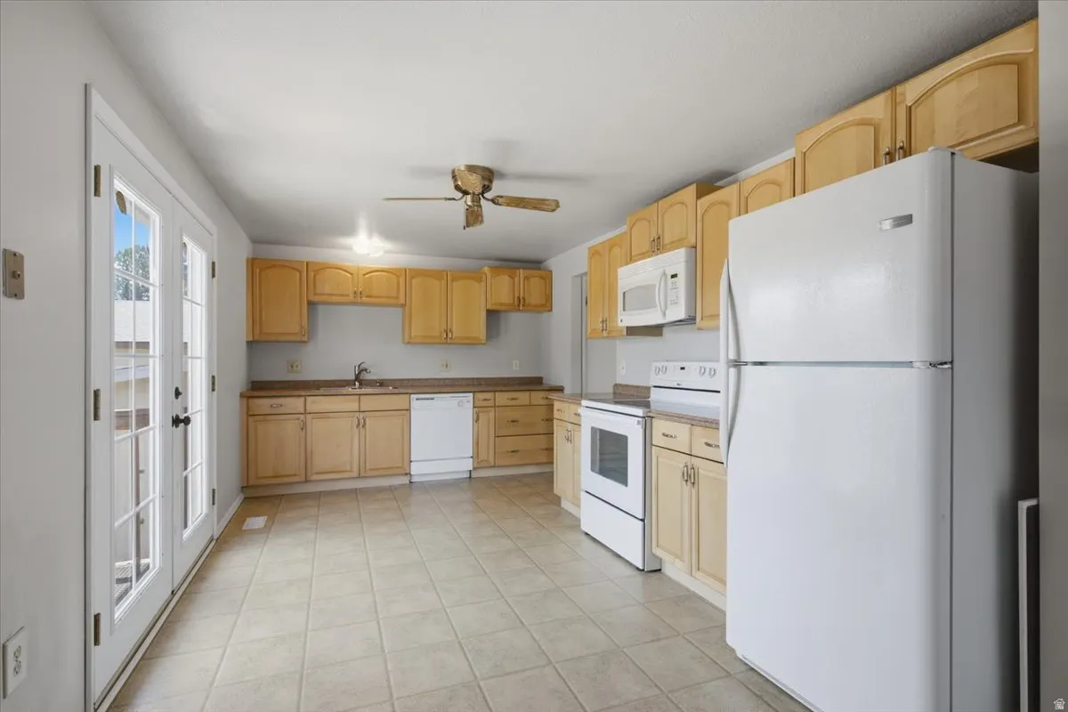 Bright kitchen featuring light wood cabinetry, white appliances, and durable tile flooring