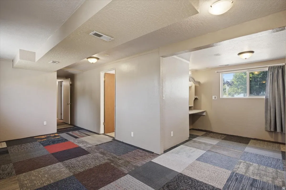 Finished basement room featuring multi-color carpet tile flooring, neutral wall paint, and recessed ceiling lighting