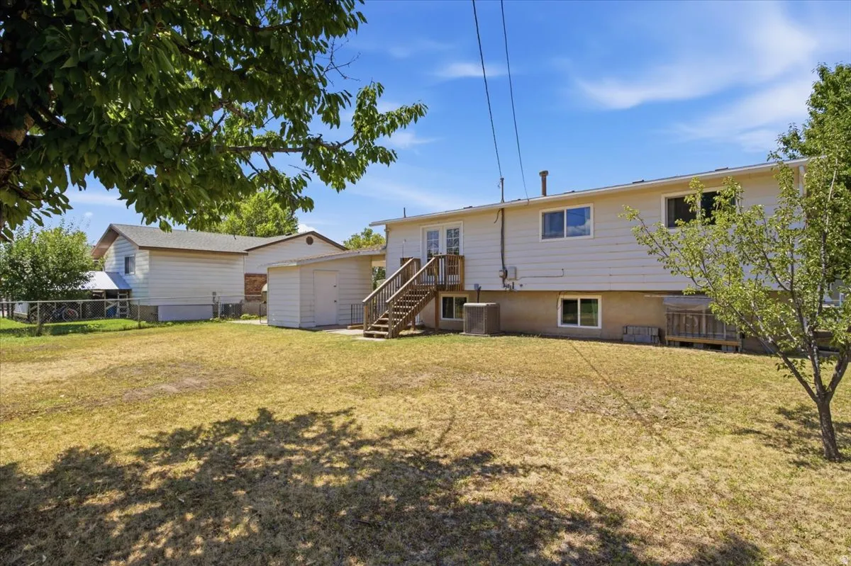 Expansive backyard featuring a large lawn area, a two-story residence with white siding, a wooden deck with stairs, multiple windows, and an outbuilding