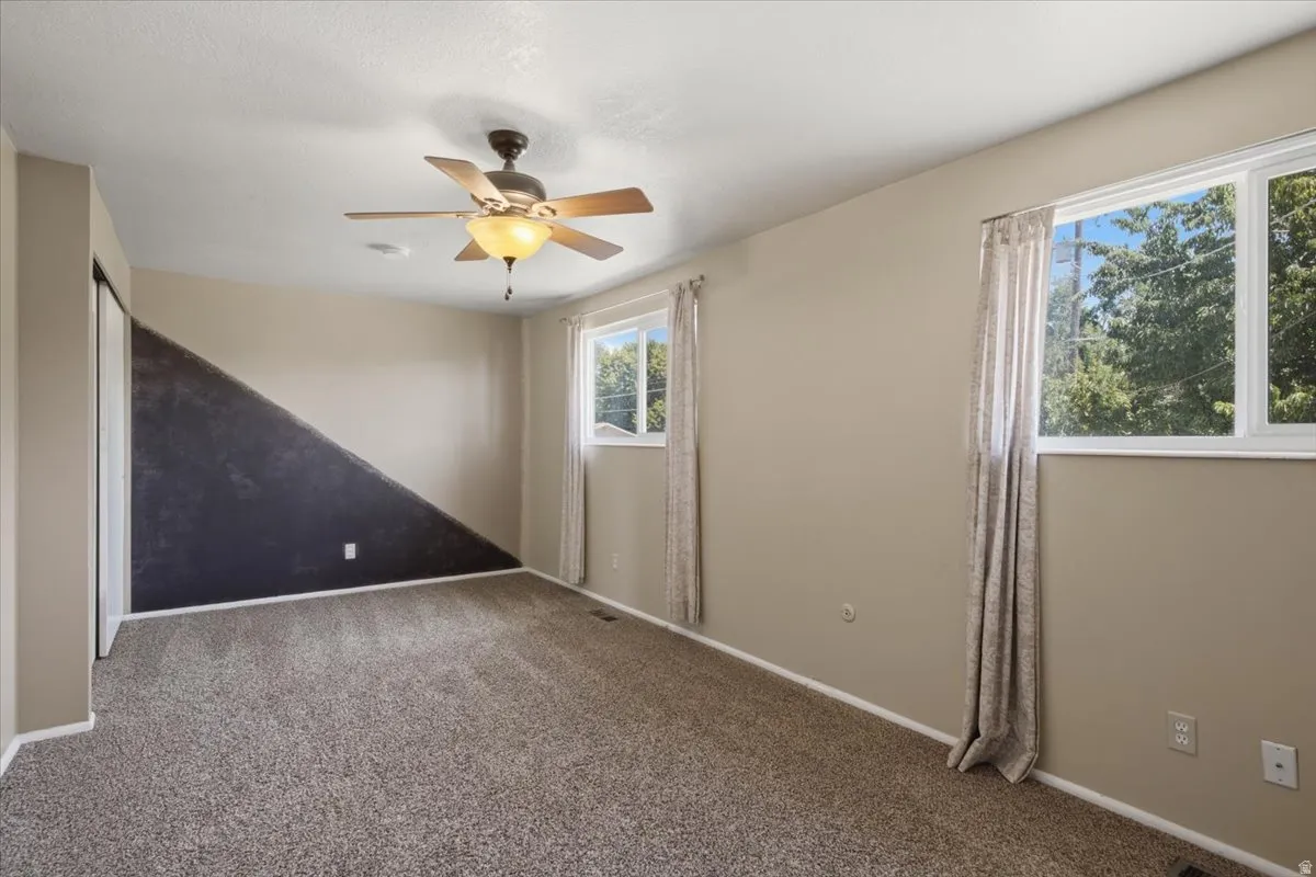 Carpeted room featuring a ceiling fan with integrated lighting, two windows, and a closet with sliding doors